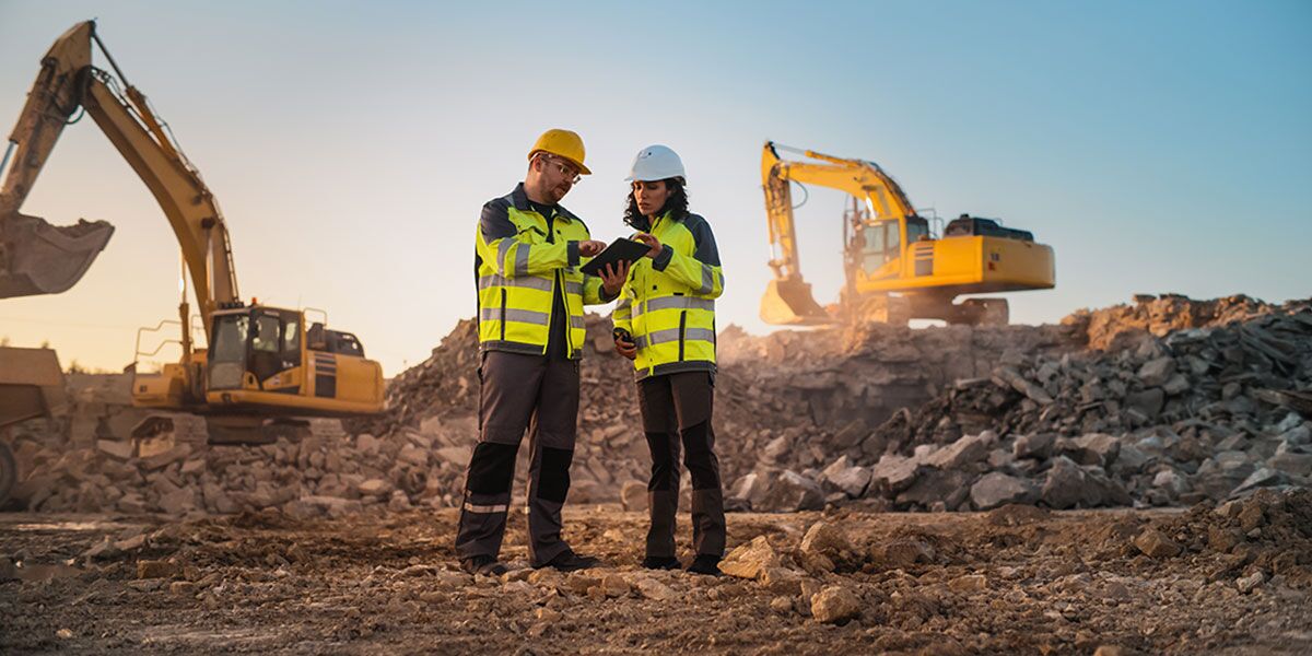 Mining workforce management blog-General Purpose Two civil engineers stand at mine site in front of two excavators